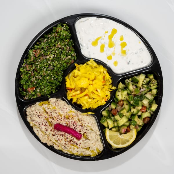 A black platter with five compartments filled with tabbouleh, tzatziki, pickled vegetables, baba ghanoush, and cucumber salad.