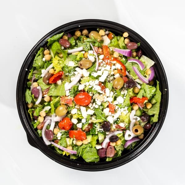 Overhead view of a vibrant Greek salad in a black bowl, with lettuce, olives, feta, and chickpeas.