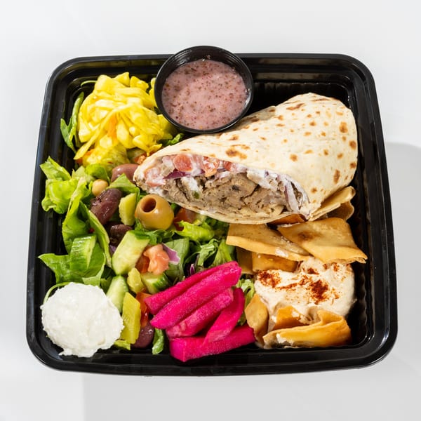 A black takeout container filled with a gyro wrap, salad, pickled vegetables, hummus, and sauce.