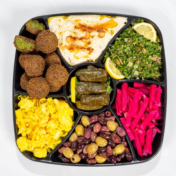 A black platter with falafel, hummus, tabbouleh, stuffed grape leaves, pickled vegetables, and olives.