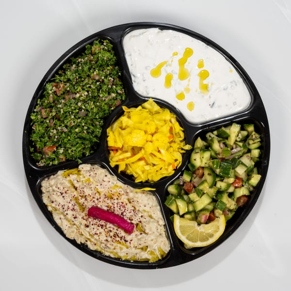 A black platter with five sections of Middle Eastern appetizers, including tabbouleh, baba ghanoush, and cucumber salad.