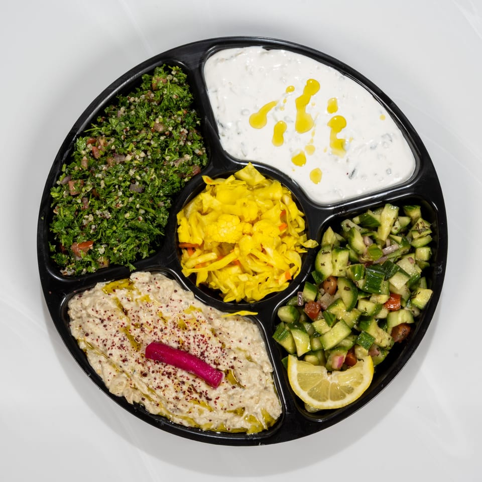 A black platter with five sections of Middle Eastern appetizers, including tabbouleh, baba ghanoush, and cucumber salad.